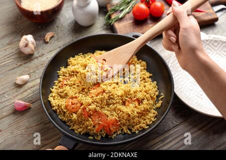 Femme mettant pilaf dans l'assiette de la poêle sur bois tableau Banque D'Images