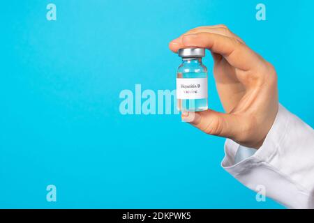 Un médecin ou un technicien de laboratoire tient un flacon avec un vaccin contre l'hépatite B dans sa main. Avec un emplacement pour le texte sur fond bleu. Banque D'Images