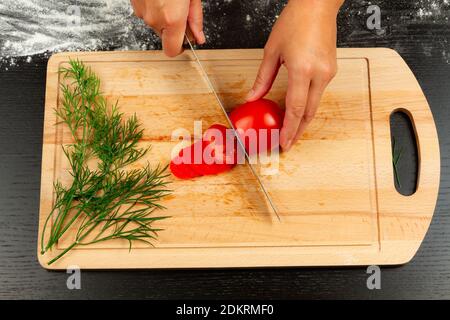 le chef cuisinier de fille coupe des tomates fraîches parfumées pour faire de la pizza italienne sur une cuisine en bois Banque D'Images