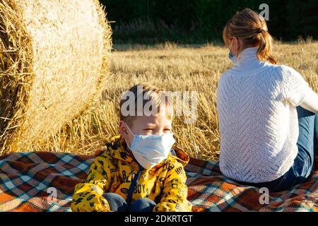 maman et bébé s'assoient sur le sol dans la nature le fond des haystacks dans les masques médicaux Banque D'Images