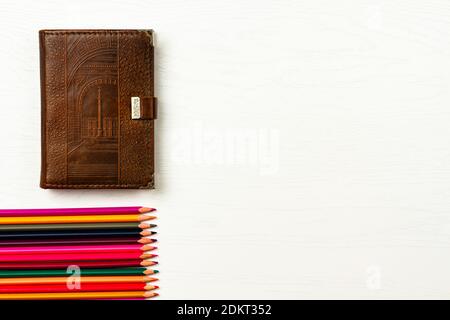 les crayons de couleur et le carnet en cuir marron se trouvent sur un blanc table en bois Banque D'Images