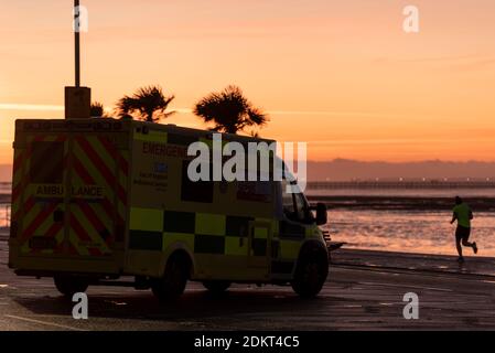 Southend on Sea, Essex, Royaume-Uni. 16 décembre 2020. En plus de Londres, certaines régions d'Essex sont entrées dans le statut d'alerte très élevée de niveau 3 après minuit. Avant le deuxième confinement, l'autorité unitaire de Southend on Sea avait choisi de rester au niveau 1 tandis que les zones environnantes d'Essex étaient au niveau 2, mais cette fois, le quartier a été placé au niveau 3. Les gens font de l'exercice le long du front de mer de la ville et se rendent au travail ou au shopping. Un homme faisant un jogging le long de la promenade au lever du soleil en passant par une ambulance Banque D'Images