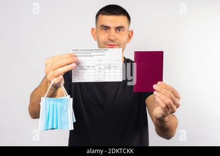 Brunette homme s'étire devant l'appareil photo une carte de vaccination, un passeport et un masque médical cassé. Un concept des conditions épidémiques pour le tourisme. Haute q Banque D'Images