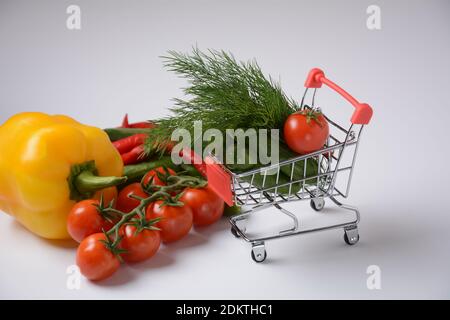 Gros plan du chariot de poussée d'épicerie de supermarché pour faire du shopping avec des concombres, des tomates, du poivron et de l'aneth sur fond blanc. Concept de shopping. Copier Banque D'Images