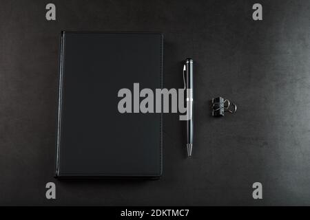 Bloc-notes noir avec un stylo noir sur fond noir. Vue de dessus, concept minimaliste. Espace libre. Banque D'Images