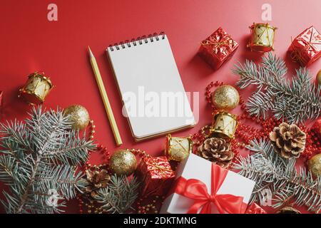 Bloc-notes et crayon pour écrire des voeux et des cadeaux pour le nouvel an et Noël autour des décorations d'arbre de Noël sur un fond rouge. Nouvel an moo Banque D'Images