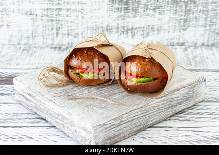 Hamburger au saumon sain avec avocat et tomate servi dans l'artisanat papier sur fond en bois Banque D'Images