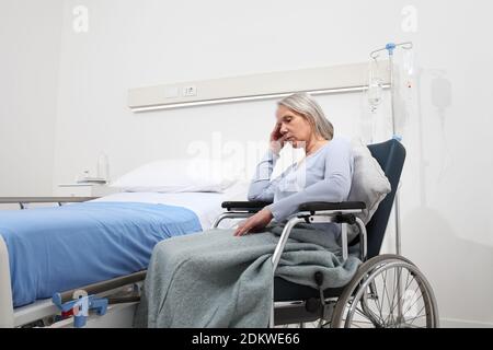 triste et pensive femme âgée abandonnée et oubliée isolée sur un fauteuil roulant près du lit dans la chambre d'hôpital, concept de solitude et de vieillesse Banque D'Images