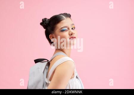 La jeune fille à la mode porte un sac à dos, posant isolé sur fond rose. Banque D'Images