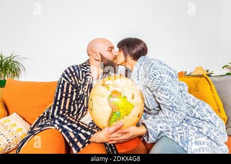 couple heureux d'un homme bald de hipster et brunette caucasien femme embrassant et tenant le globe terrestre assis à l'aise sur un canapé.plan de voyage, togethernes Banque D'Images