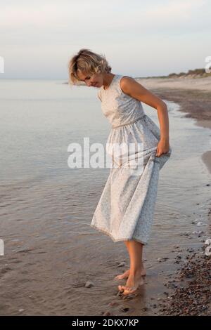 Femme en robe marche pieds nus dans l'eau par le mer Banque D'Images