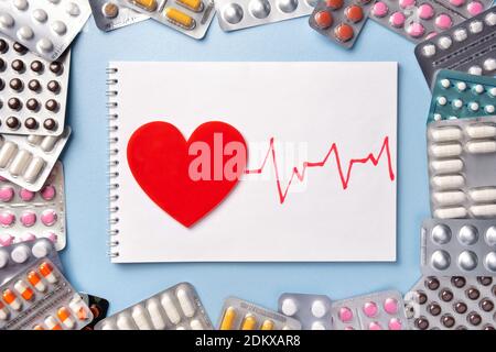 Bouquet de pilules de différentes couleurs dans blisters sur fond bleu avec carnet. Cœur avec électrocardiogramme ou ecg et diagramme de pouls. Pharmacie Banque D'Images