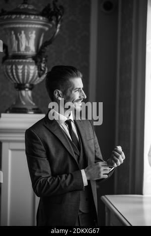 Marié le jour du mariage souriant et attendant la mariée dans le hall de l'hôtel. Élégant homme riche en costume et noeud papillon. Banque D'Images