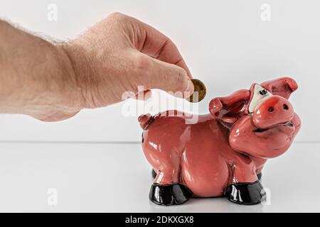 Male hand throws a coin into a piggy bank and euro coins on a white background. Keeping money and investment concept. Selective focus Stock Photo