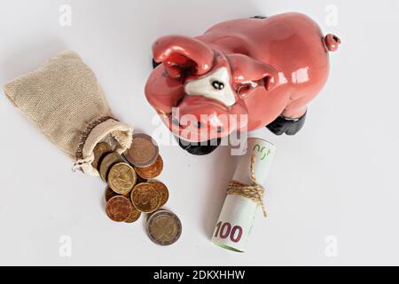 Les pièces en euros tombent du burlap et des billets de papier roulés avec la banque de porc sur un fond blanc. Mise au point sélective Banque D'Images