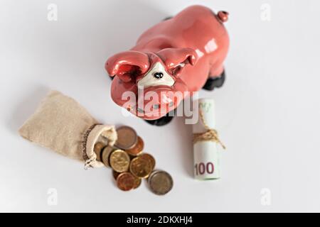 Les pièces en euros tombent du burlap et des billets de papier roulés avec la banque de porc sur un fond blanc. Mise au point sélective Banque D'Images