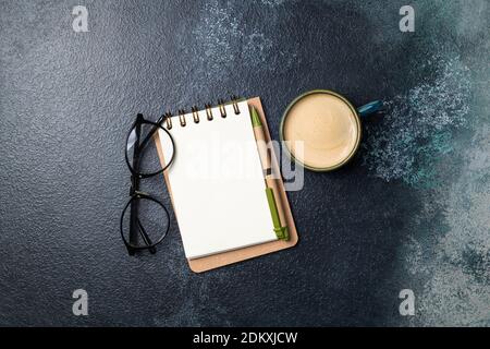 Carnet blanc vierge et tasse à café sur table de bureau. Bureau de travail avec accessoires d'affaires, bloc-notes ouvert et tasse de café. Espace de copie, vue de dessus Banque D'Images