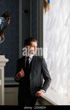 Marié le jour du mariage souriant et attendant la mariée dans le hall de l'hôtel. Élégant homme riche en costume et noeud papillon. Banque D'Images