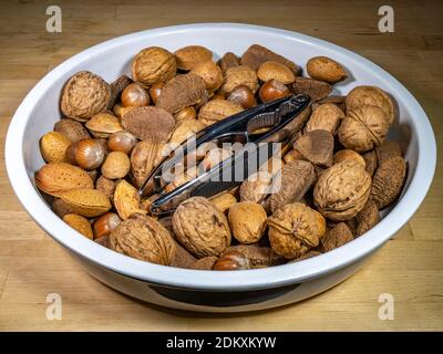 Gros plan POV de fruits à coque mélangés entiers (amandes, noisettes et noix) dans un bol, avec une paire de casse-noisettes sur le dessus. Banque D'Images