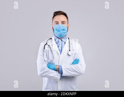 Médecin professionnel en uniforme, masque facial et gants en caoutchouc posé sur fond gris studio Banque D'Images