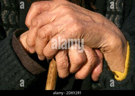 Gros plan des mains d'une femme âgée reposant sur une canne Dans la campagne roumaine Banque D'Images