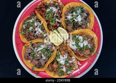 Vue en hauteur de l'assortiment plateau d'échantillons de tacos de rue chargé de poulet, porc al pasteur, steak asada, et présenté sur une assiette rouge. Banque D'Images