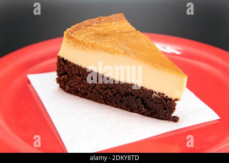 Couche de chocolat au fond du dessert Flan mexicain coupée en coin et présentée sur une assiette rouge. Banque D'Images