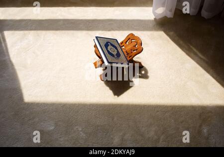 Quran Koran holy book with silver embossing at wooden stand in room with sun light, muslim pray, islamic home Stock Photo