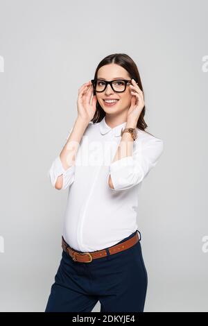 jeune femme d'affaires souriante enceinte dans des lunettes isolées sur le gris Banque D'Images