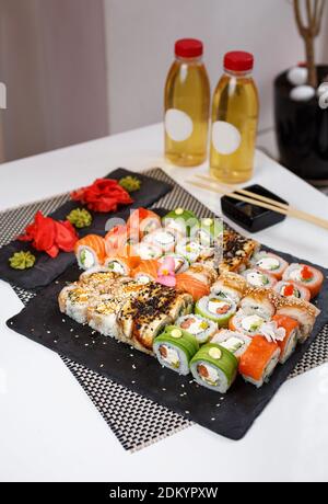 Différents types de sushis japonais, petits pains et maki avec sauce, wasabi et gingembre. Sur un tableau sombre sur une table blanche. Banque D'Images