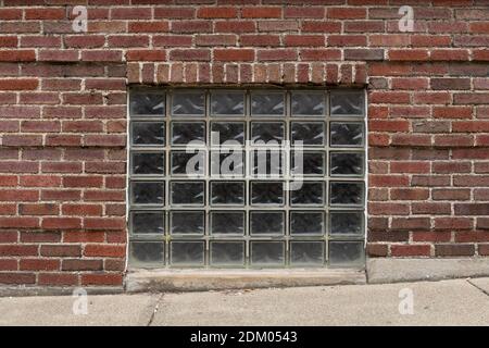 Vue directe d'une fenêtre de sous-sol avec blocs de briques de verre incrustées, trottoir en béton sur une pente, aspect horizontal Banque D'Images