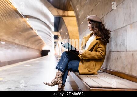 femme élégante en béret et automne magazine de lecture de vêtements plate-forme metro Banque D'Images