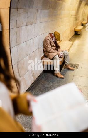 homme senior en tenue d'automne dormant sur un banc de plate-forme de métro sur un premier plan flou Banque D'Images