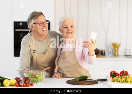 Joyeux conjoints âgés faisant Selfie avoir plaisir à cuisiner dans la cuisine Banque D'Images