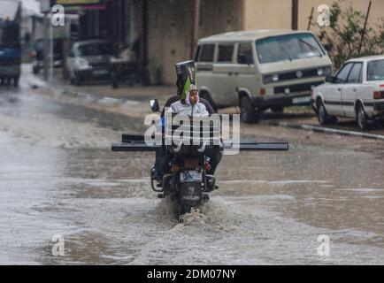 Gaza, Palestine. 16 décembre 2020. Un palestinien roule à moto avec un enfant devant une route inondée dans le nord de la bande de Gaza. Crédit : SOPA Images Limited/Alamy Live News Banque D'Images