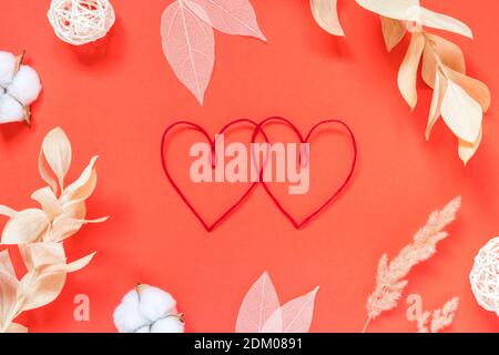 Saint-Valentin, amour, concept romantique. Coeurs rouges et différentes fleurs séchées sur fond rouge. plat. Banque D'Images