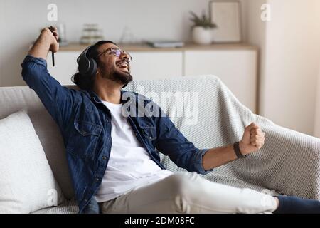 Détente à la maison. Joyeux Guy de l'est écoutant de la musique dans des écouteurs et dansant à la maison Banque D'Images