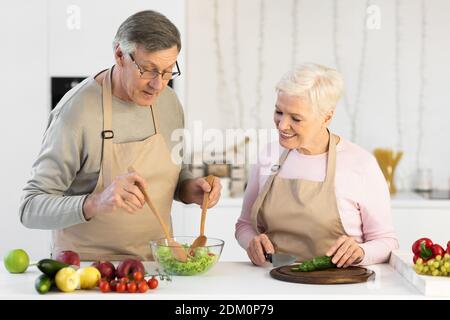 Conjoints âgés préparer une salade de légumes saine pour le dîner dans la cuisine Banque D'Images