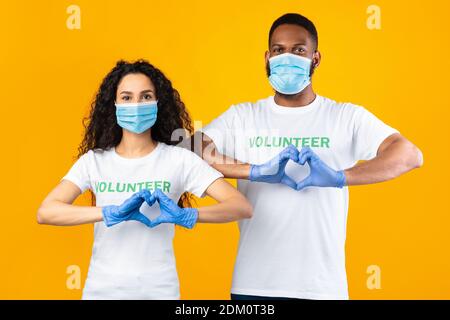 Deux volontaires en gestant en forme de coeur portant des masques et des gants, fond jaune Banque D'Images