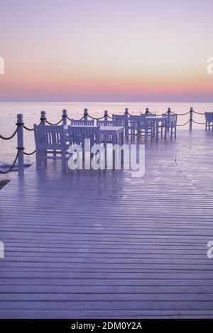 Lever du soleil, coucher de soleil les lumières pourpre et orange se reflètent sur la table et la chaise en bois blanc légèrement humide à l'embarcadère d'Antalya Turquie. Banque D'Images