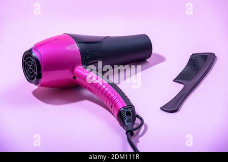 Sèche-cheveux, peigne et brosse à cheveux sur fond rose. Coiffeur professionnel. Outils nécessaires pour le soin des cheveux. Banque D'Images