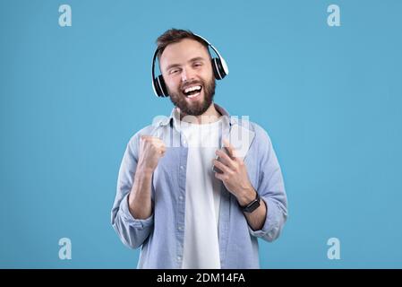 Beau homme avec téléphone portable écoutant de la musique dans des écouteurs, chantant avec sa chanson préférée sur fond bleu Banque D'Images