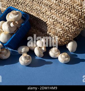 Sur une table bleue, il y a un sac en osier et des champagnes dans une boîte en plastique bleu et des champignons en vrac. Banque D'Images