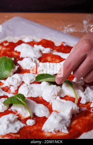 Un plan vertical d'un cuisinier mettant une feuille dessus La pâte à pizza Artisan à la mozzarella et à la sauc de tomate Banque D'Images