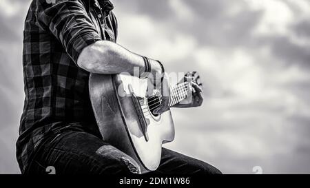 Les mains de l'homme jouant de la guitare acoustique, gros plan. Guitares acoustiques en train de jouer. Concept de musique. Noir et blanc Banque D'Images