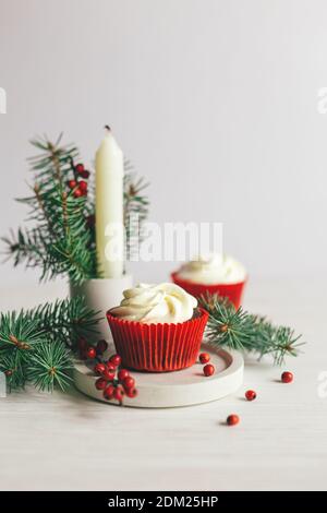 Délicieux petits gâteaux décorés de branches d'épicéa et de baies rouges sur fond blanc. Bonbons pour la fête de Noël. Séjour écologique Banque D'Images