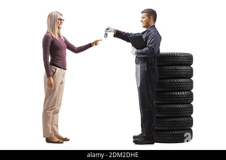Mécanicien automobile avec une pile de pneus donnant des clés de voiture à une cliente blonde souriante isolée sur fond blanc Banque D'Images