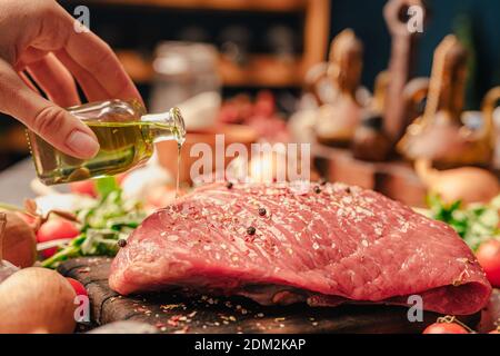 Assaisonnement à la main de femme avec de l'huile d'olive extra vierge et épices une viande de veau coupée ronde pour un dîner rôti. Préparer une grande partie de viande pour un groupe Banque D'Images