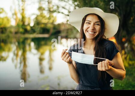 Joyeuse femme souriante tenant un masque hygiénique dans la nature. Femme protégée. Fin du concept de pandémie de coronavirus.femme célébrant sans masque.Covid-19 vir Banque D'Images