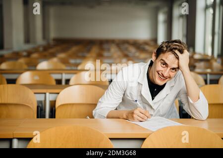 Étudiant souriant et compétent prenant un examen facile dans un amphithéâtre vide. Un étudiant optimiste qui fait un test en classe. Femme heureuse ayant le stress fr Banque D'Images